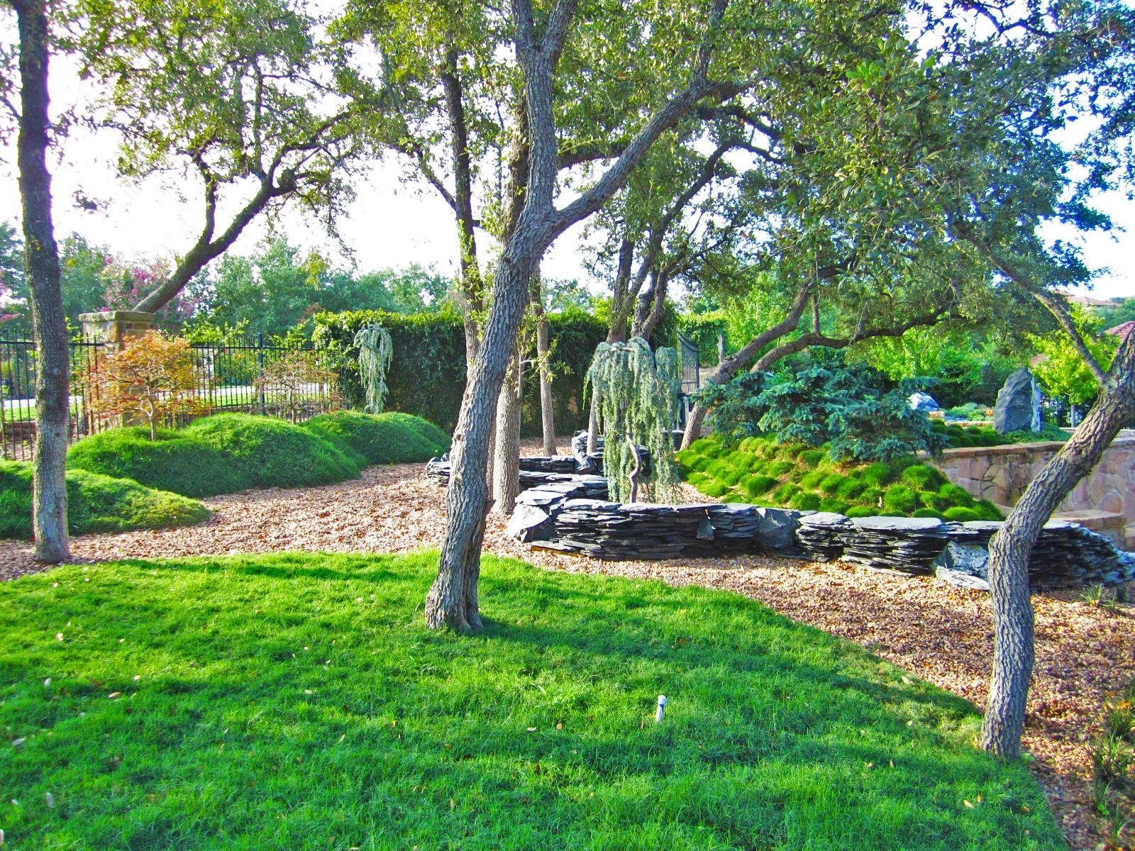 Lush green garden with trees, bushes, and a pathway with stone features.