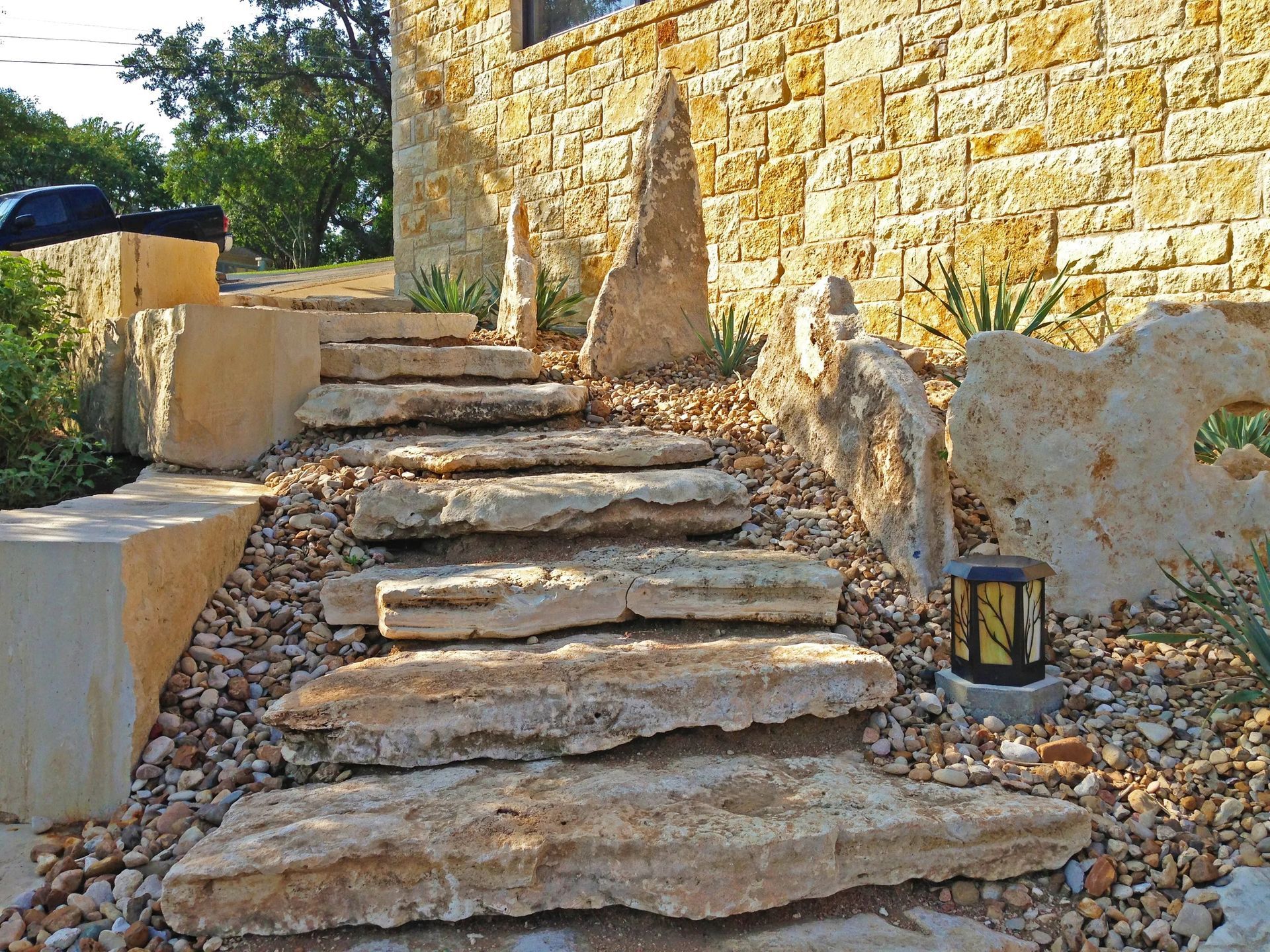 Rustic stone steps lead up to a golden-hued stone building, accented by decorative boulders and gravel landscaping.