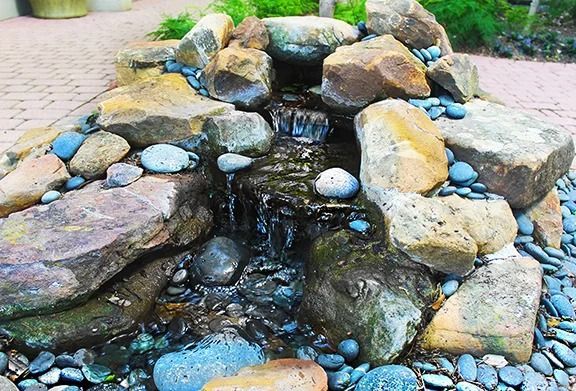 Small stone waterfall cascading over rocks, surrounded by pebbles.