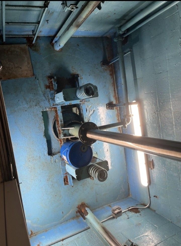 Inside a blue industrial room, pipes and a large vertical metal pole extend from the floor to the ceiling.