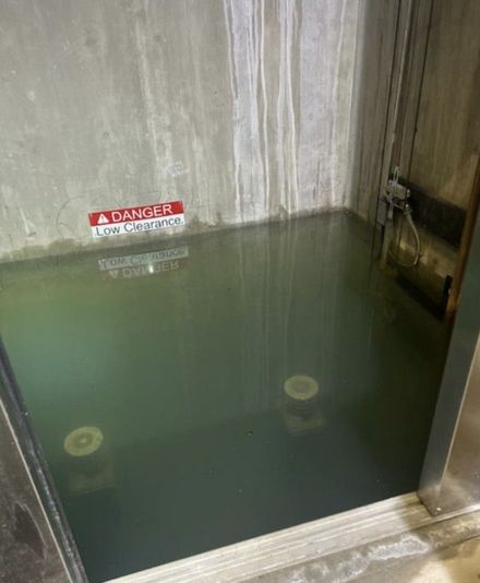 Small elevator flooded with murky water and a red danger sign on the wall
