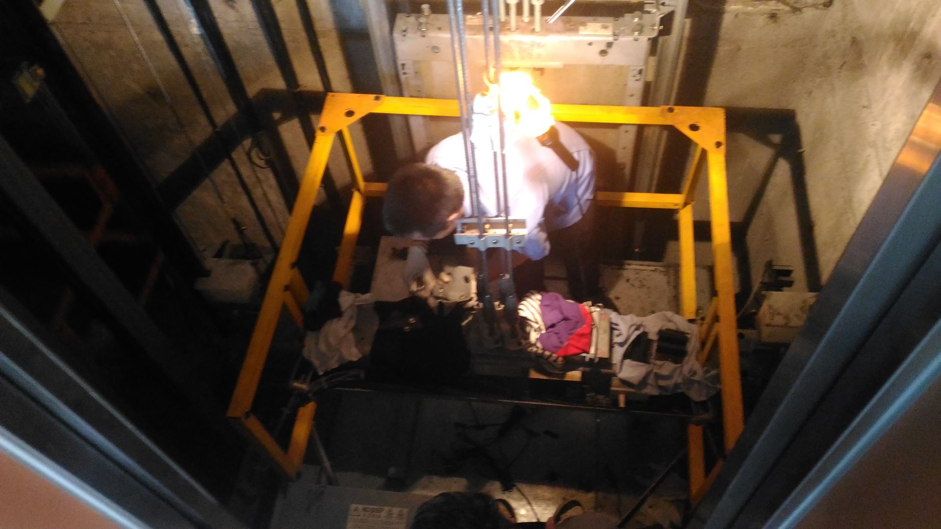 Workers on a platform inside a shaft, illuminated by a bright overhead light during construction.
