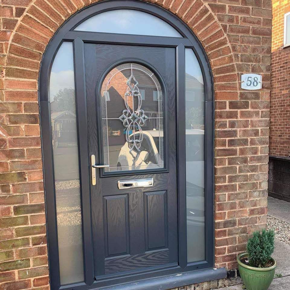 A black door with a stained glass window is on a brick building.