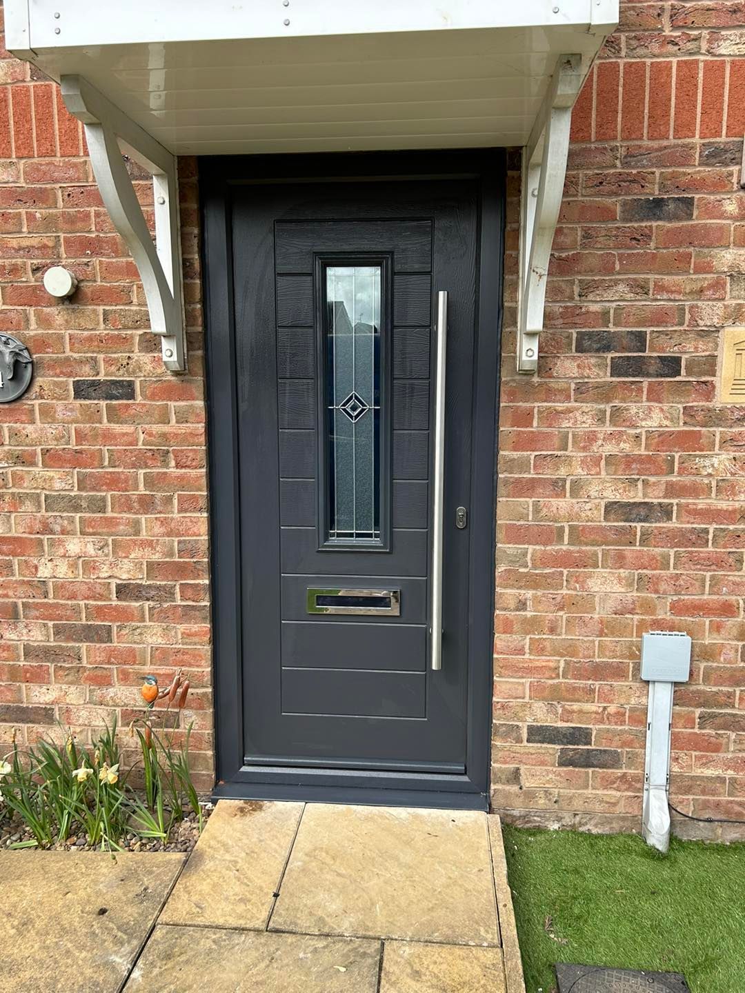 A black front door with a stainless steel handle is on a brick building.