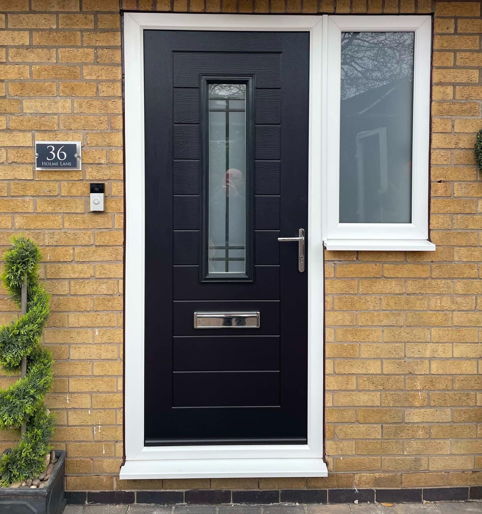 A black front door with a white trim and a window on a brick building.