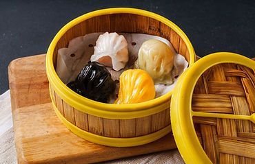 Steamed dumplings in a bamboo basket on a wooden board, with the lid beside it