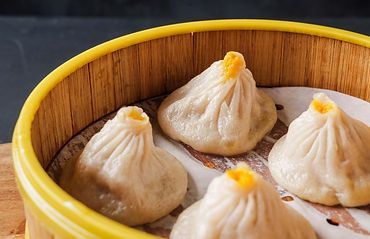 Steamed dumplings in a bamboo basket with a yellow rim, topped with orange garnish