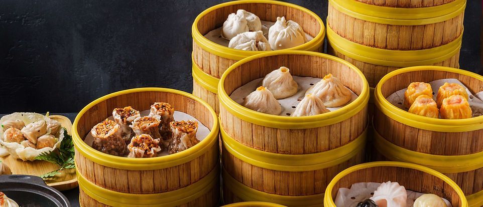 Steamed dim sum in bamboo baskets on a dark table, with assorted dumplings and buns.