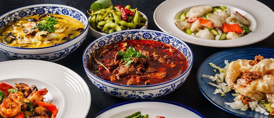 Assorted Asian dishes in patterned bowls and white plates on a dark tablecloth