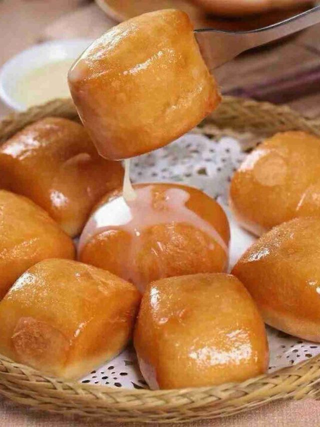 Basket of glossy golden baked buns, one lifted above the others on a lace-lined tray