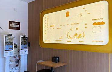 Wall-mounted healthcare monitor display with two self-service kiosks in a bright clinic hallway