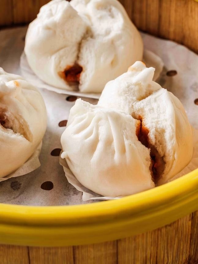 Steamed buns in a yellow basket lined with parchment paper