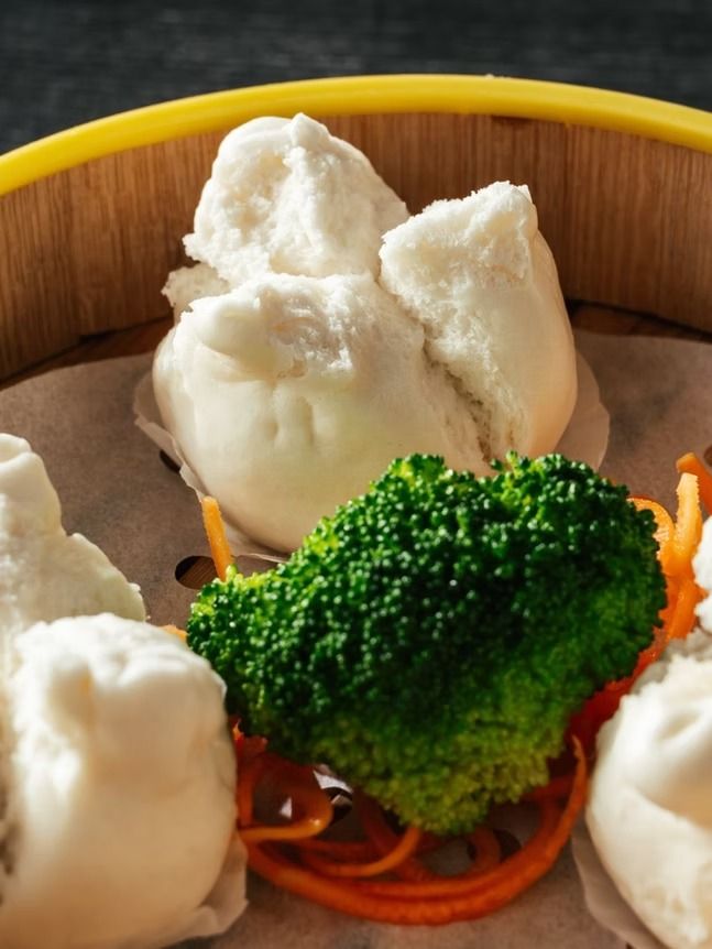 White dumplings with broccoli in a wooden bowl, with shredded carrot garnish