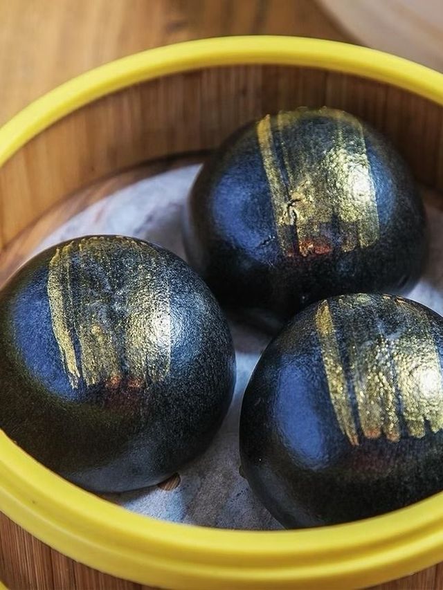 Three dark, gold-striped fruit in a yellow-rimmed bowl on a wooden surface.