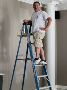 A man is standing on a ladder painting a wall