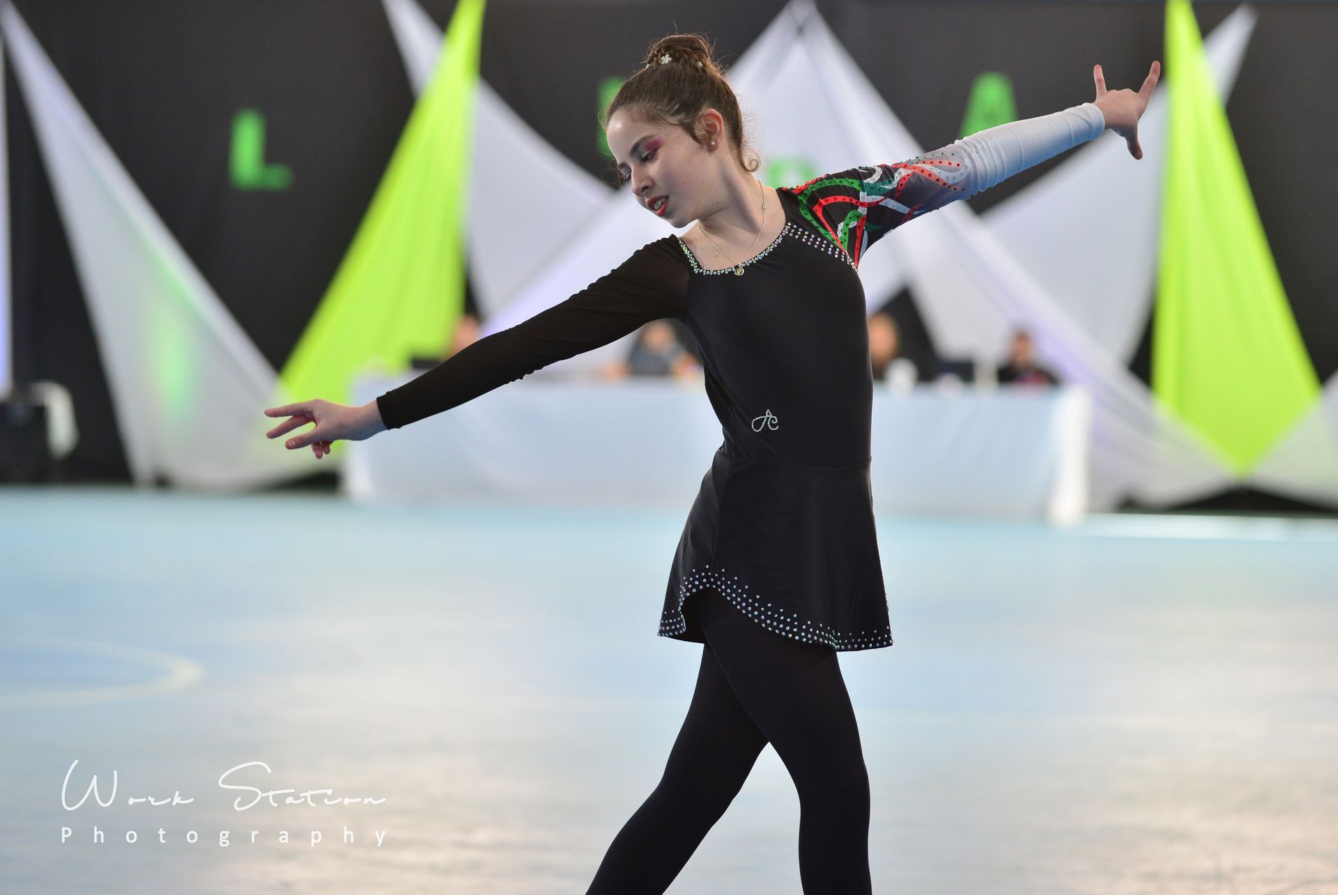 Una patinadora artística con un traje negro realiza una elegante pose con los brazos extendidos