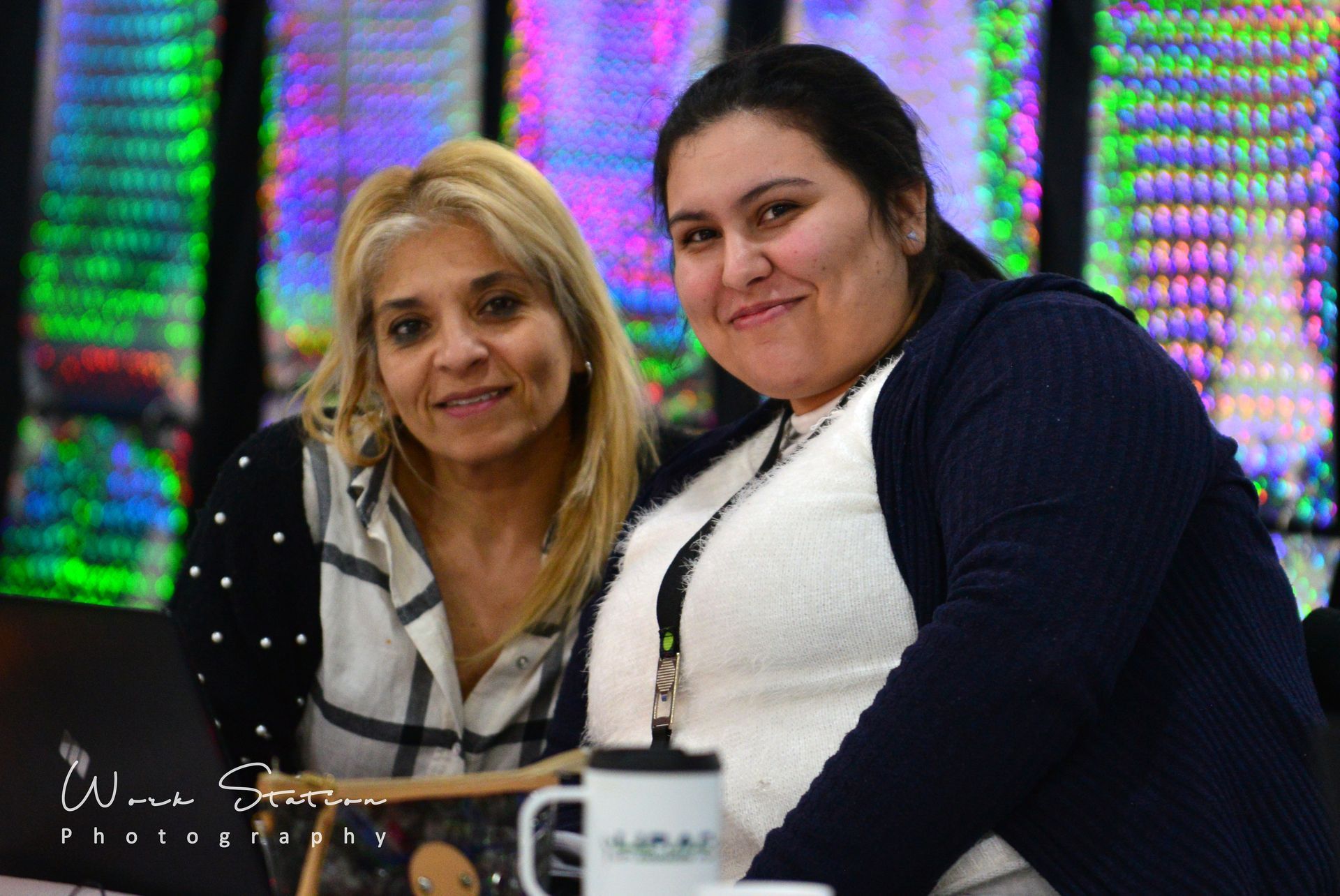 Dos personas sonríen una al lado de la otra sentadas en un escritorio 