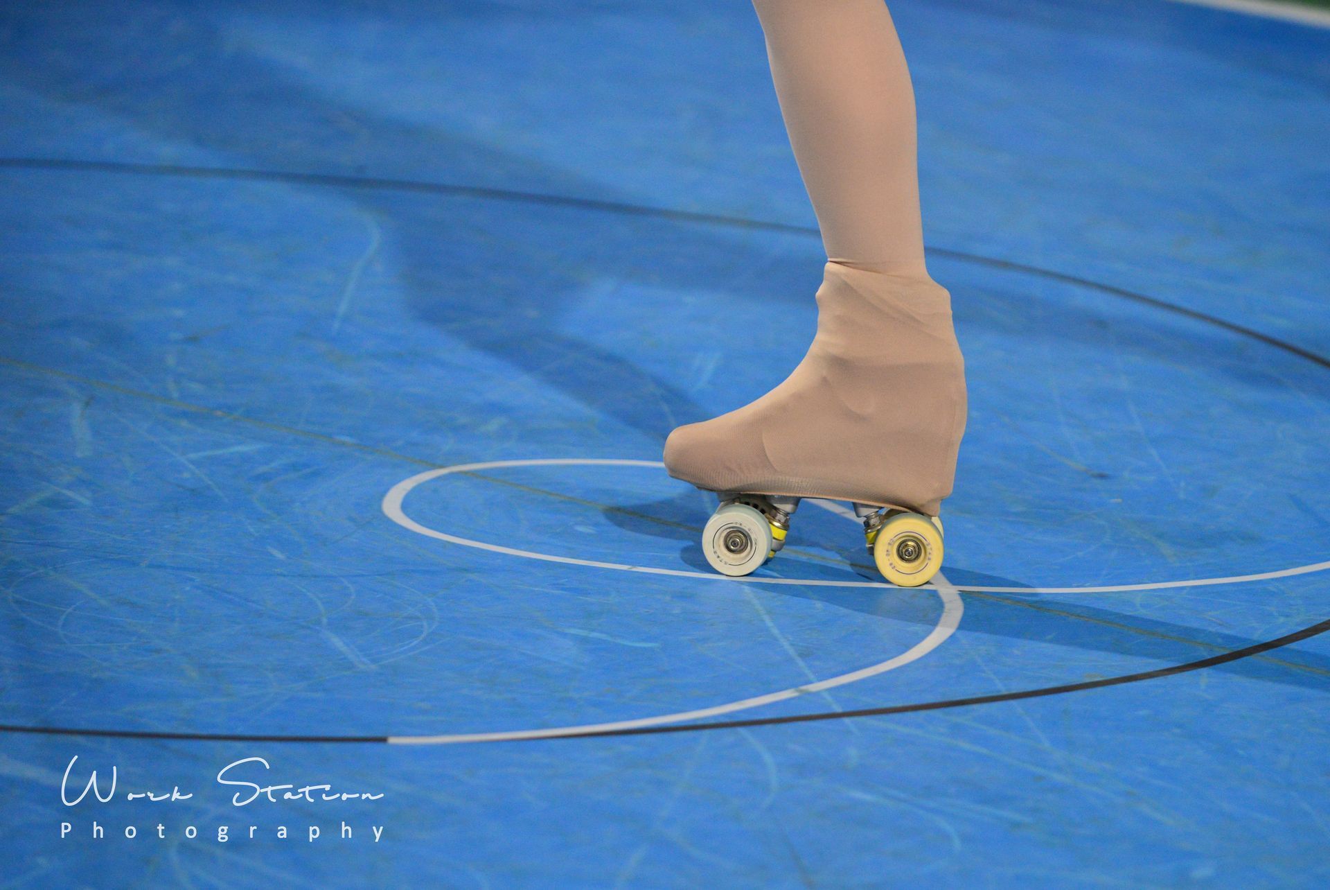 Primer plano de un patín con una bota de color beige moviéndose sobre una superficie azul con marcas blancas.