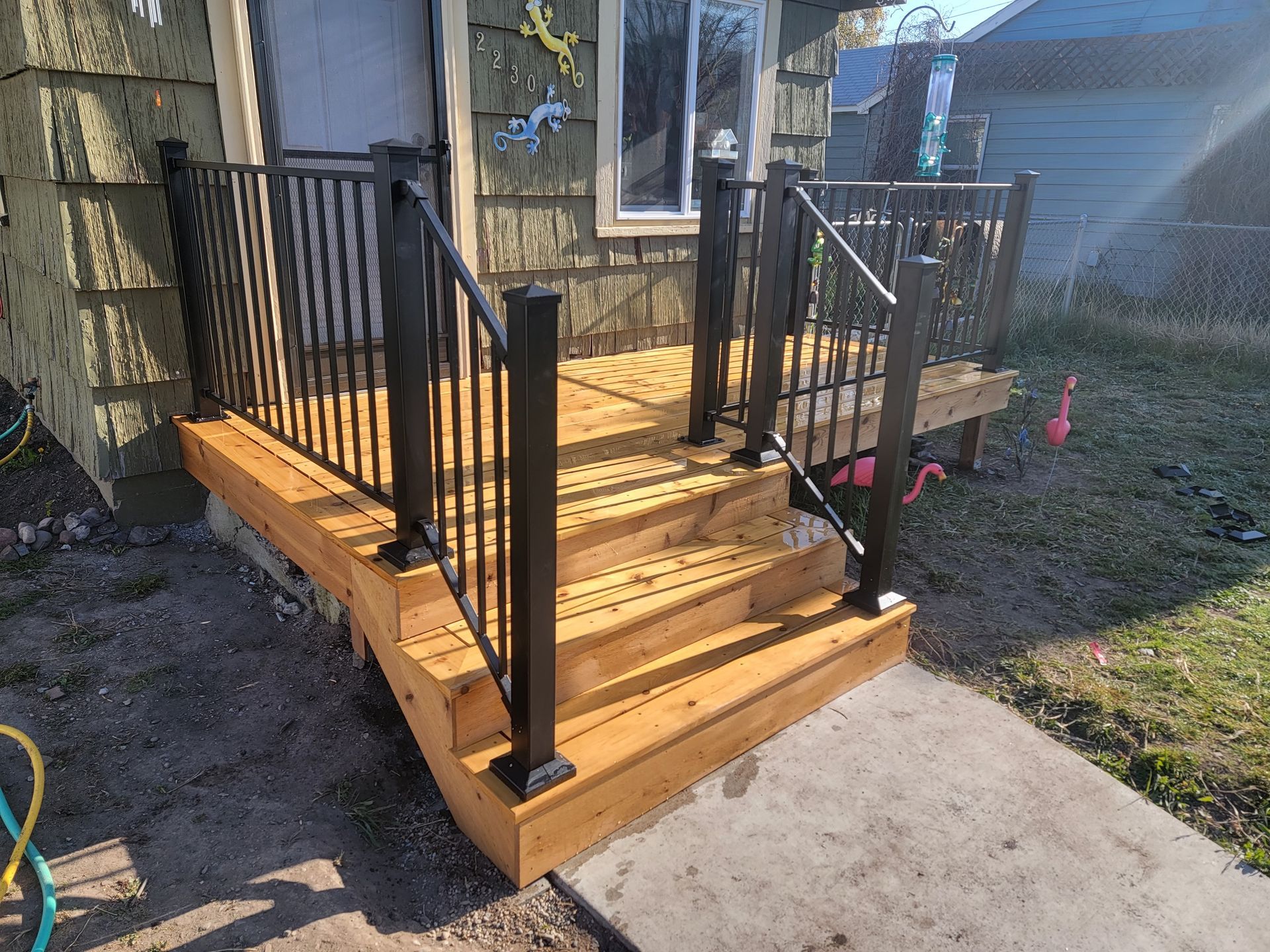 Wooden deck with black railings and steps leading to a house entrance.