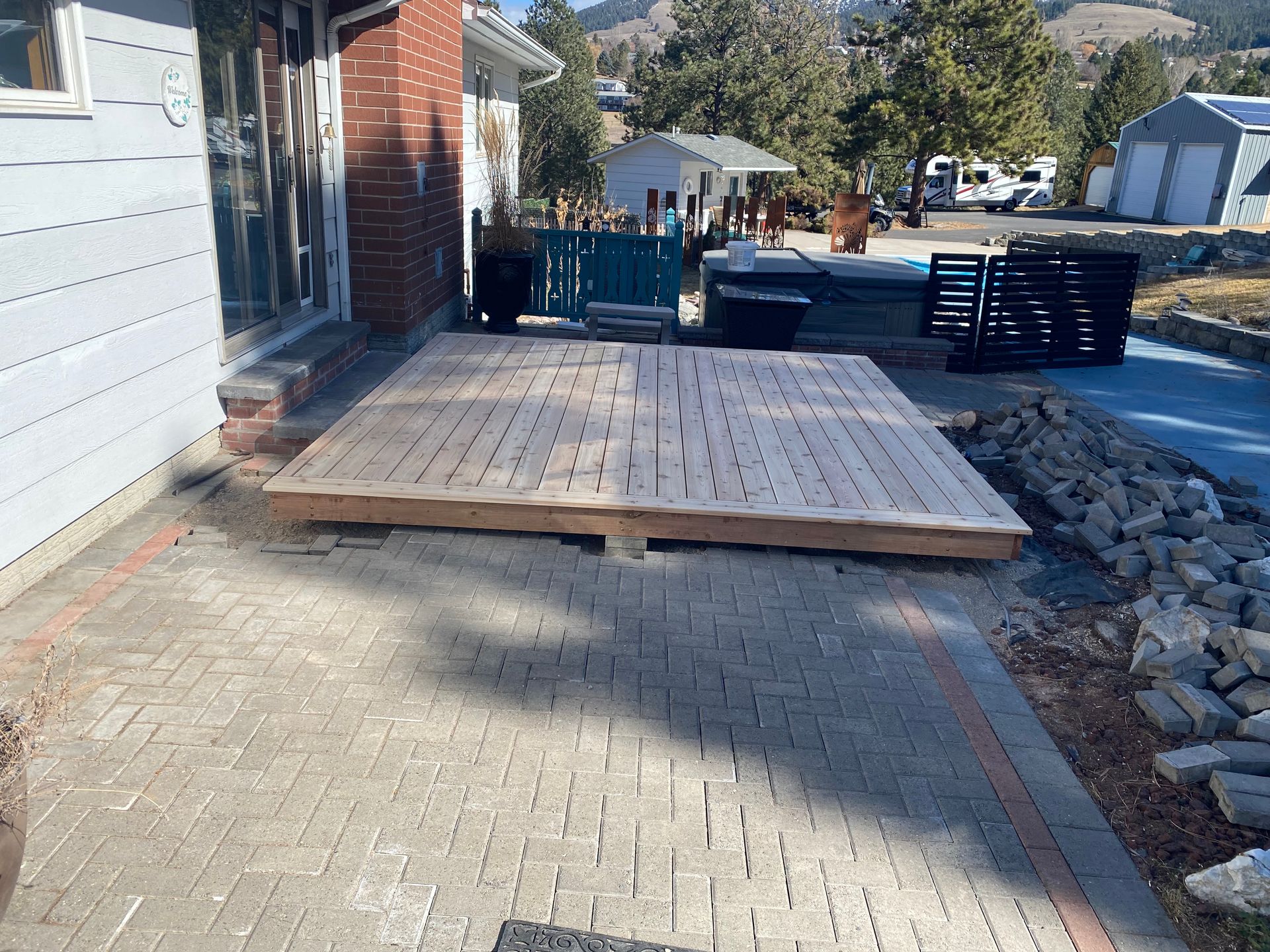 A wooden deck is sitting on a brick patio in front of a house.