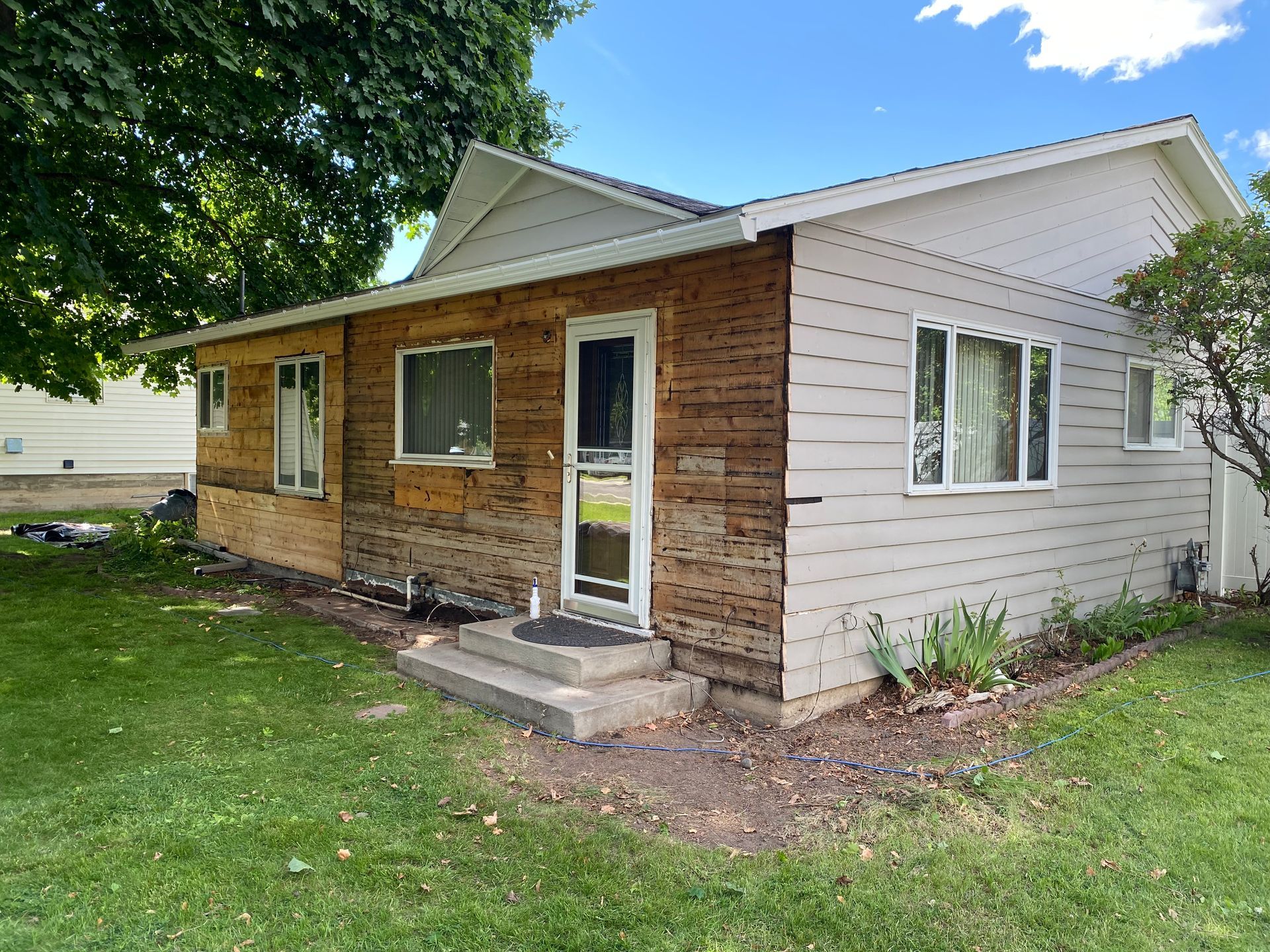 A small white house with a wooden siding is sitting on top of a lush green field.