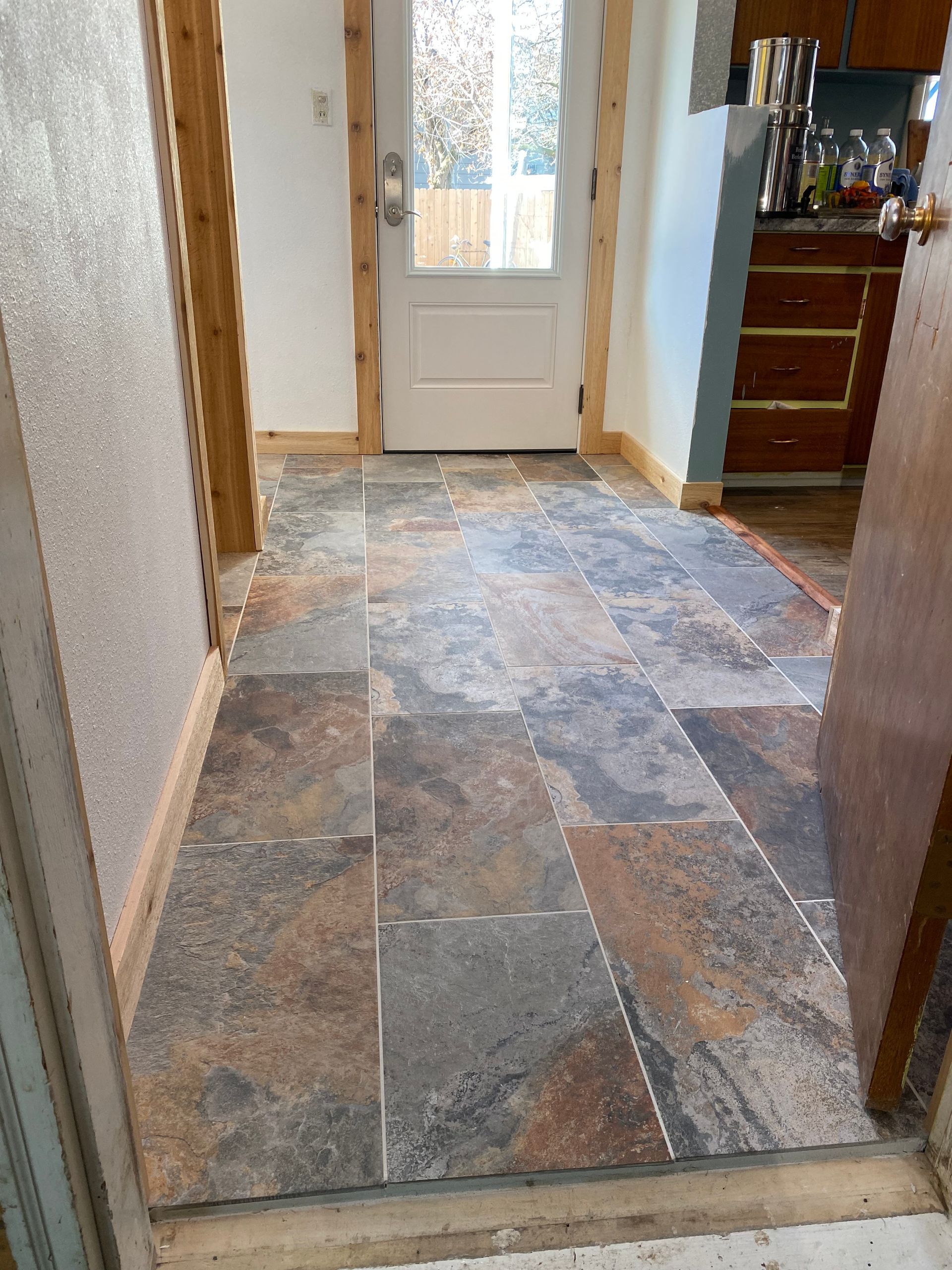 A hallway with a tiled floor and a door leading to a kitchen.