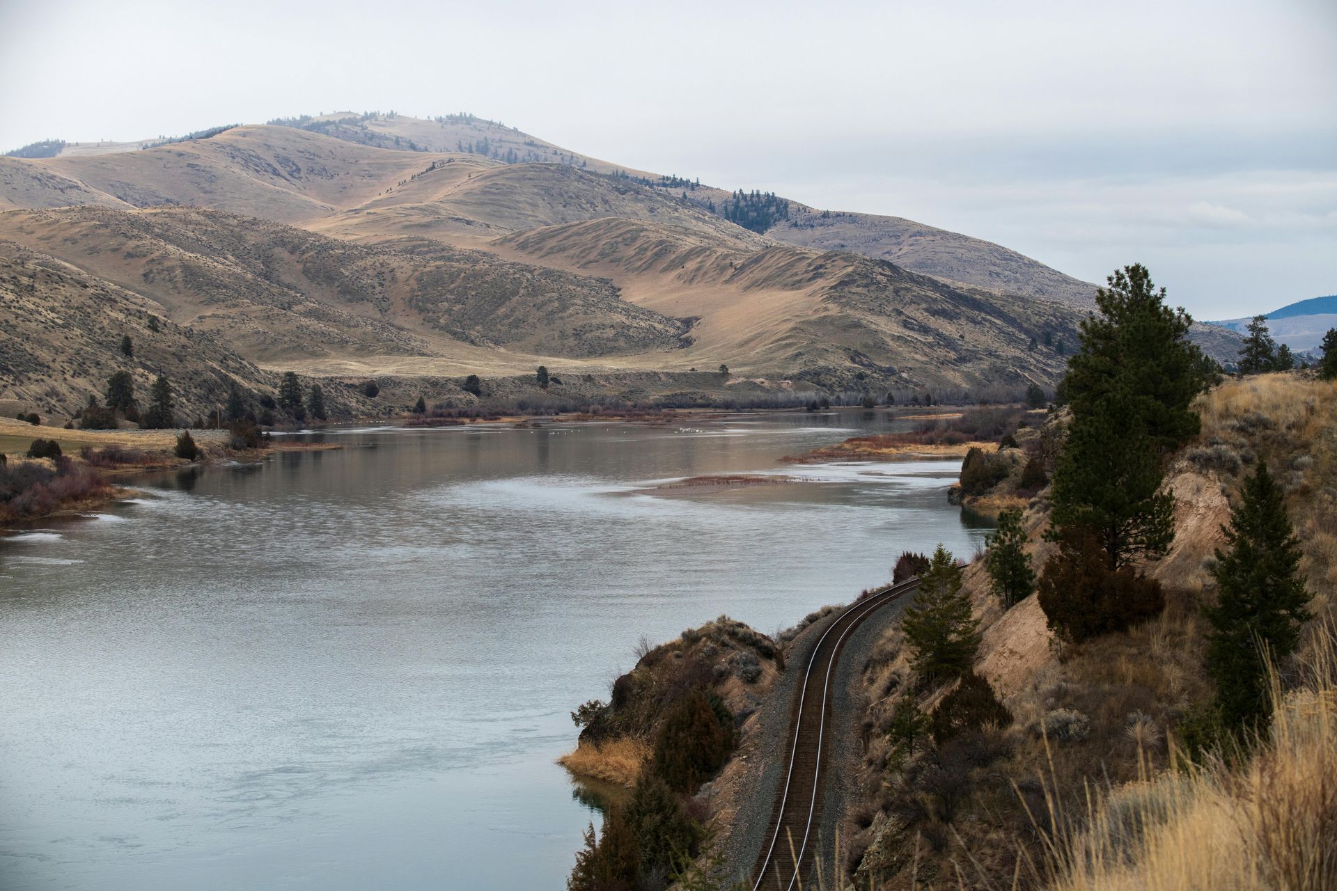 A road going through a valley next to a lake with mountains in the background.