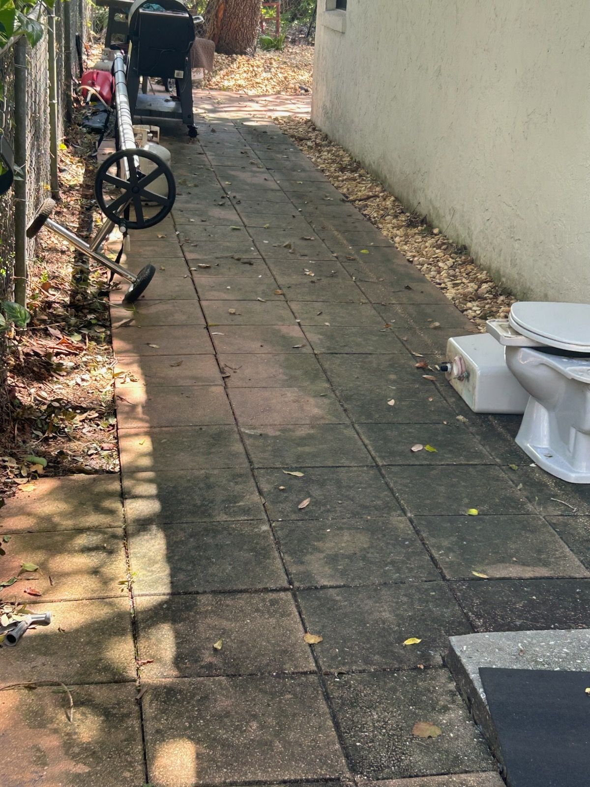 Narrow paved alleyway with a wheelbarrow and outdoor items along a wall.