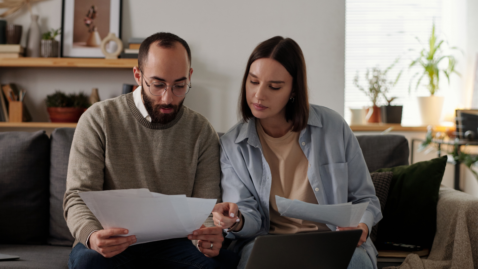 Two people on a couch reviewing documents together in a bright living room