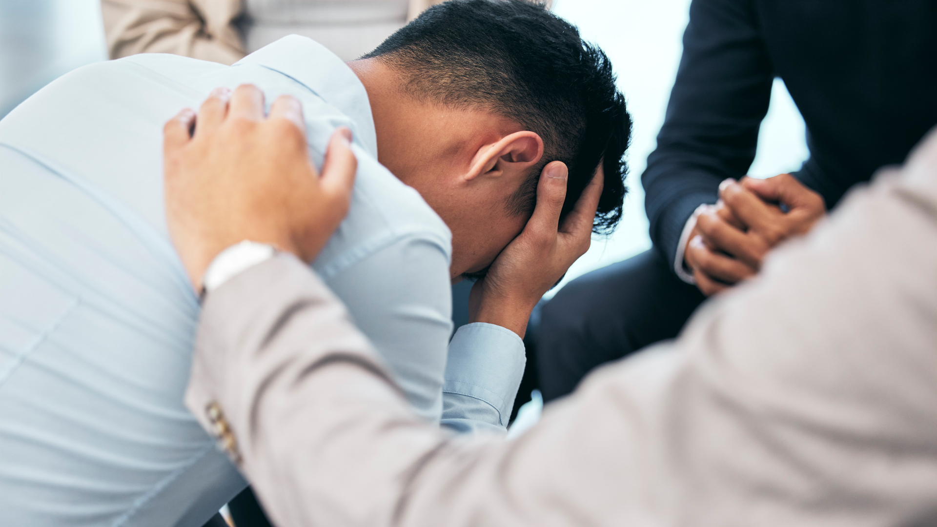Person with head in hand, comforted by others in a supportive group setting