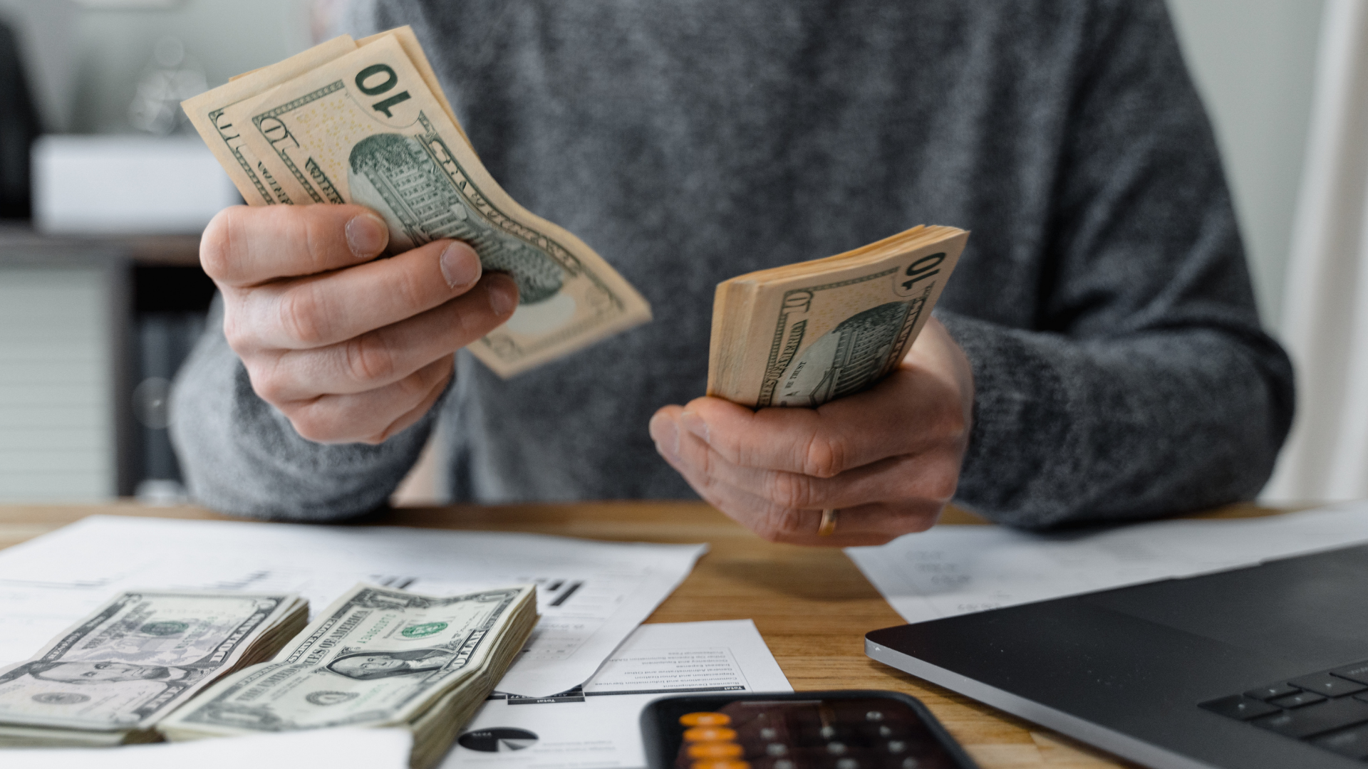 Hands counting U.S. dollar bills at a desk with a calculator and paperwork