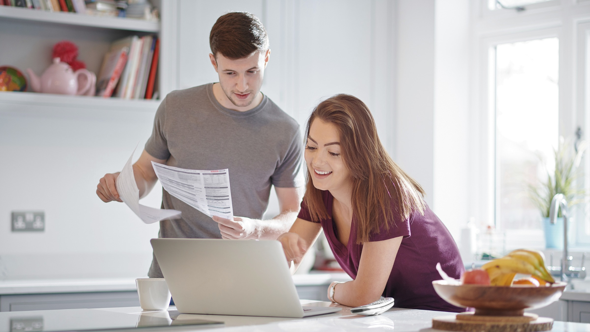Two people reviewing papers and a laptop together in a bright kitchen
