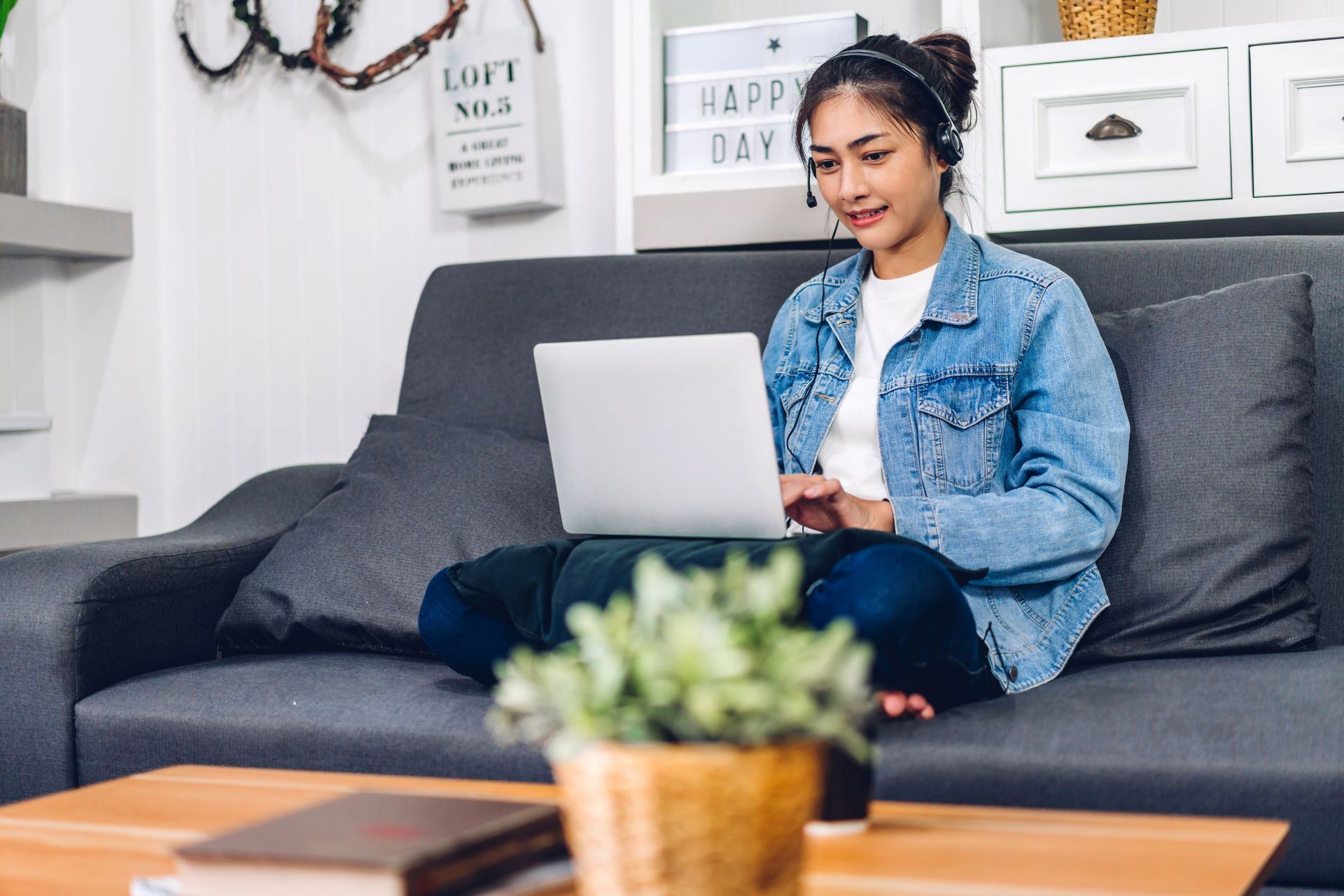 Woman using a laptop on a gray couch in a bright living room
