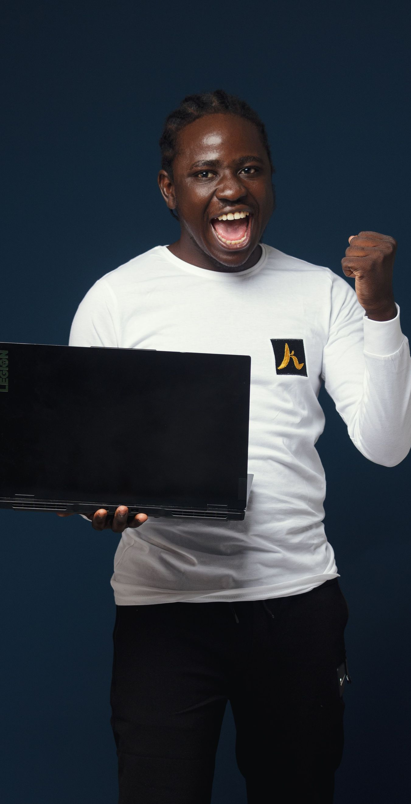 Smiling person in a white shirt holding a laptop and raising a fist against a dark background