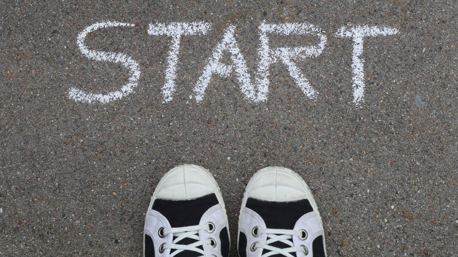 White sneakers at a chalk-drawn “START” on a pavement surface