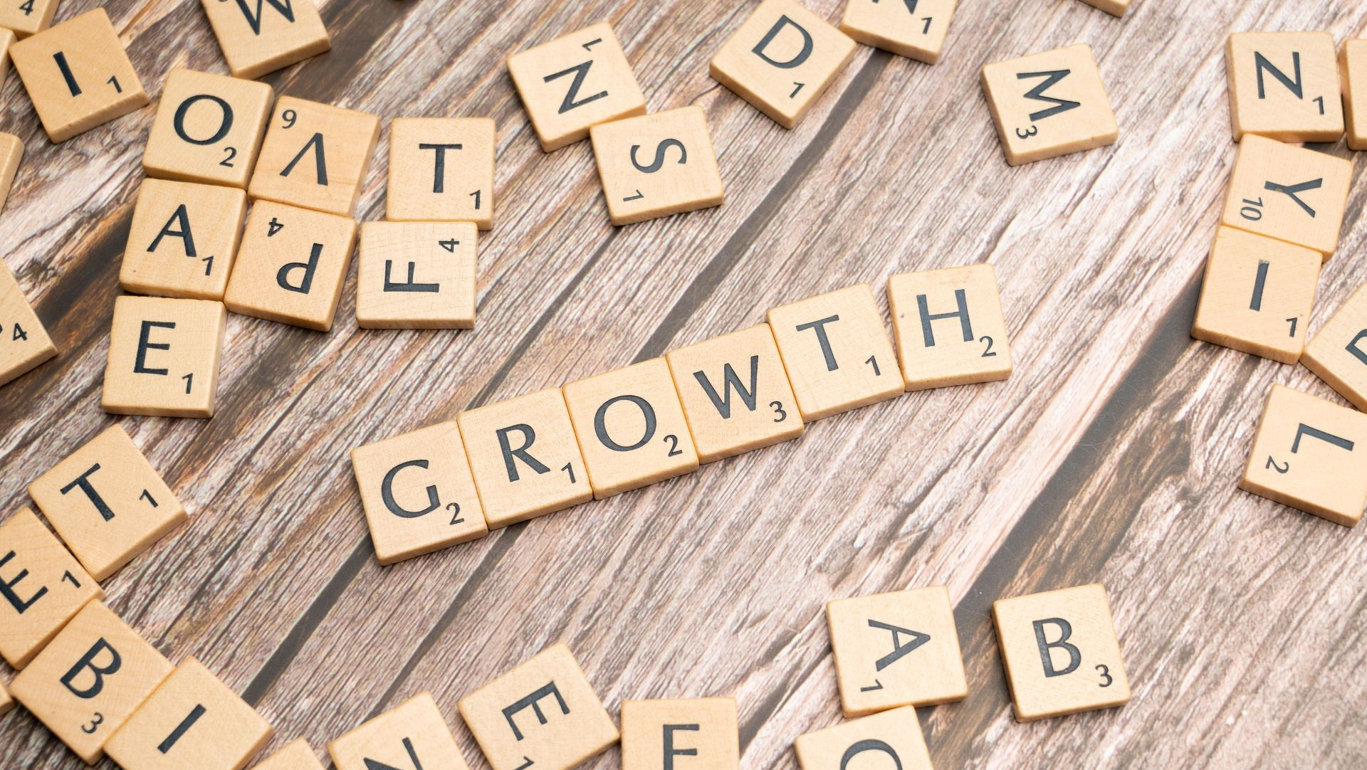 Wooden letter tiles spelling “GROWTH” on a rustic tabletop, surrounded by scattered tiles