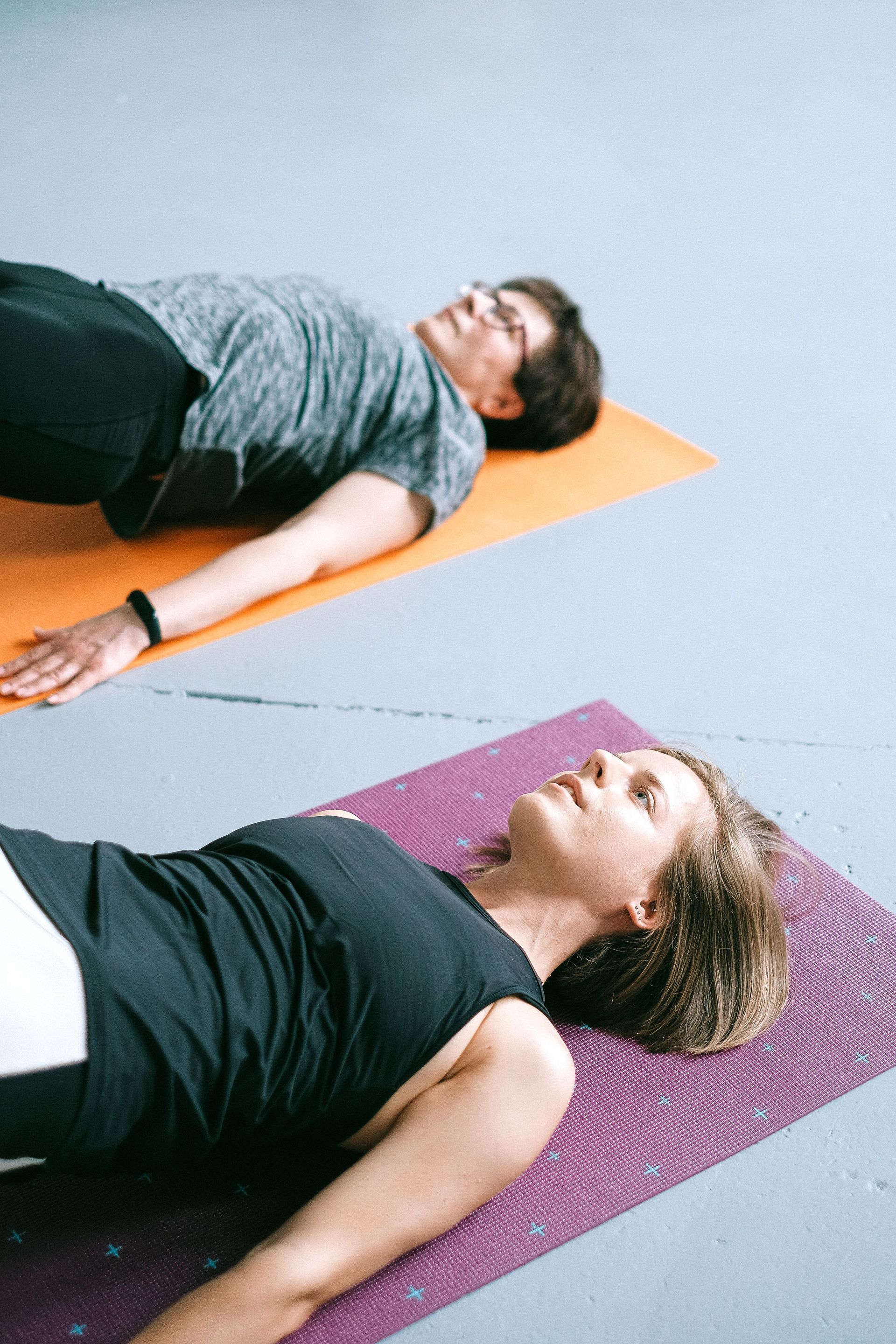 Two people lying on yoga mats, relaxed on their backs in a studio-like space