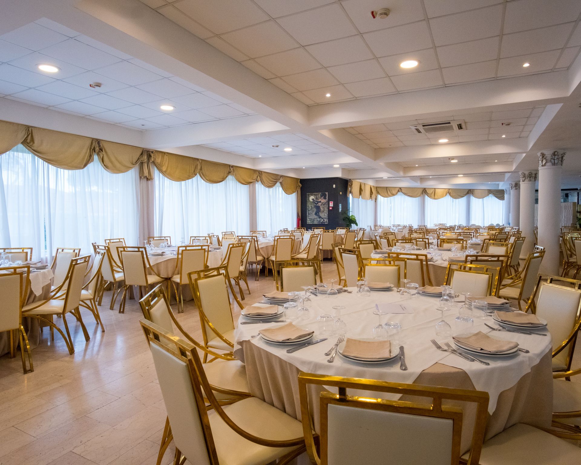 Elegante sala da pranzo del ristorante con sedie dorate, tavoli apparecchiati e una parete decorata con un mosaico.