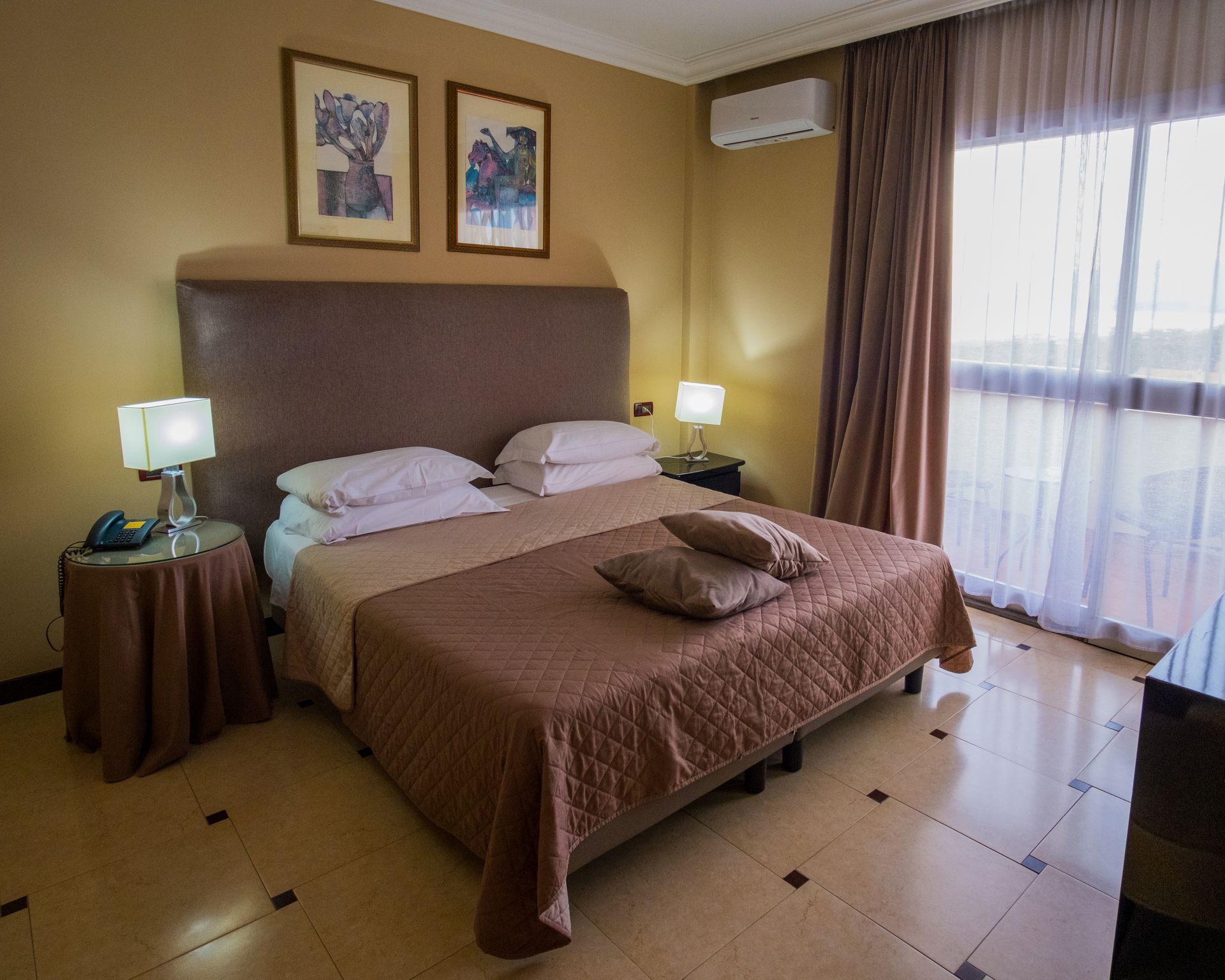 Un letto ben rifatto con lenzuola bianche e cuscini decorativi marroni in una camera da letto illuminata da una luce soffusa.