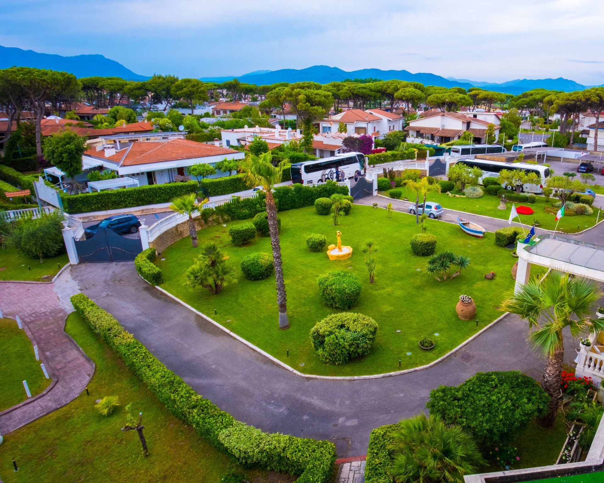 Veduta aerea di un quartiere residenziale con case dai tetti rossi, un parco verde e montagne sullo sfondo.