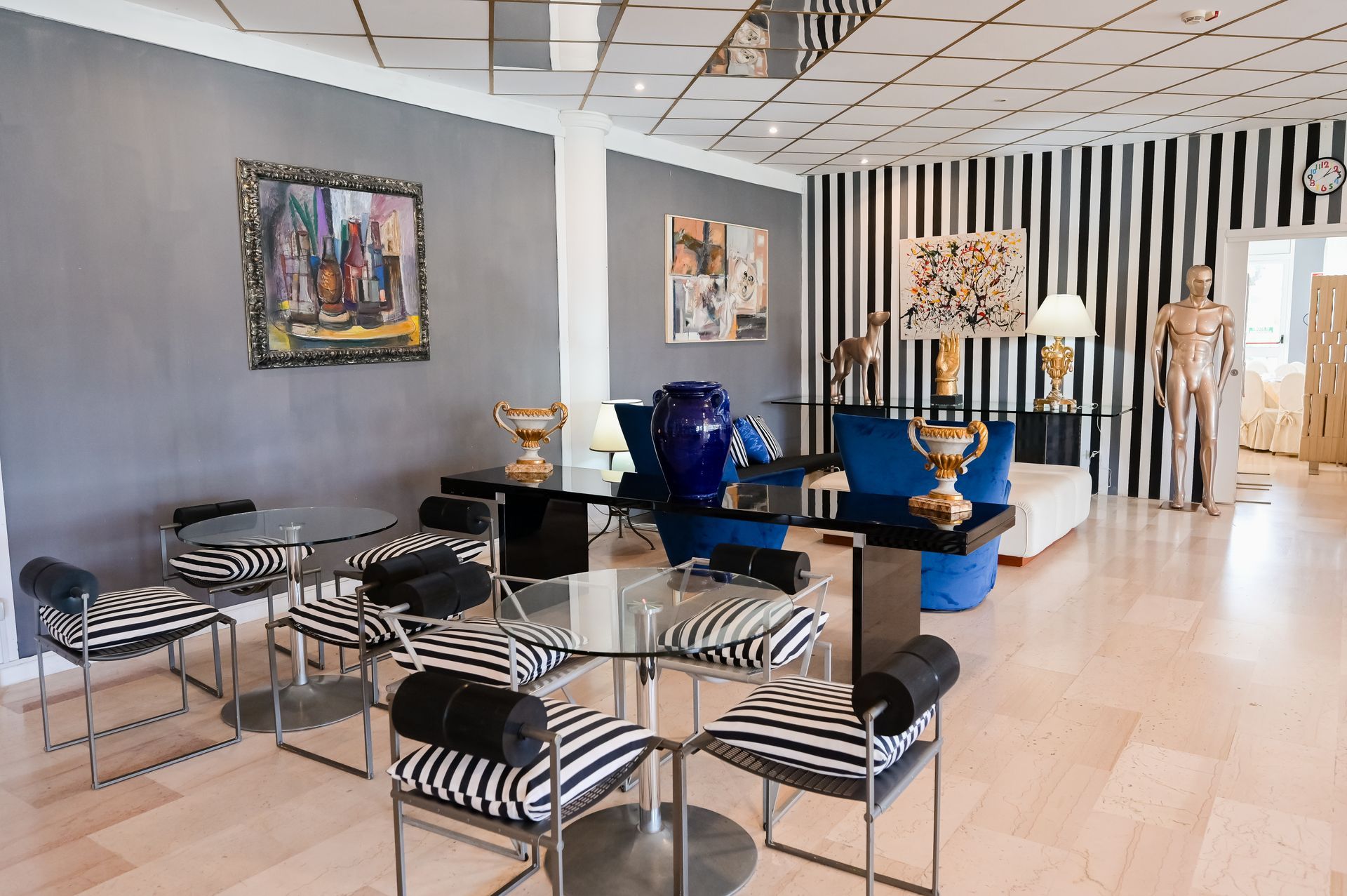 Showroom moderno con sedie a righe, vaso blu, quadri incorniciati e manichini su pareti a righe.