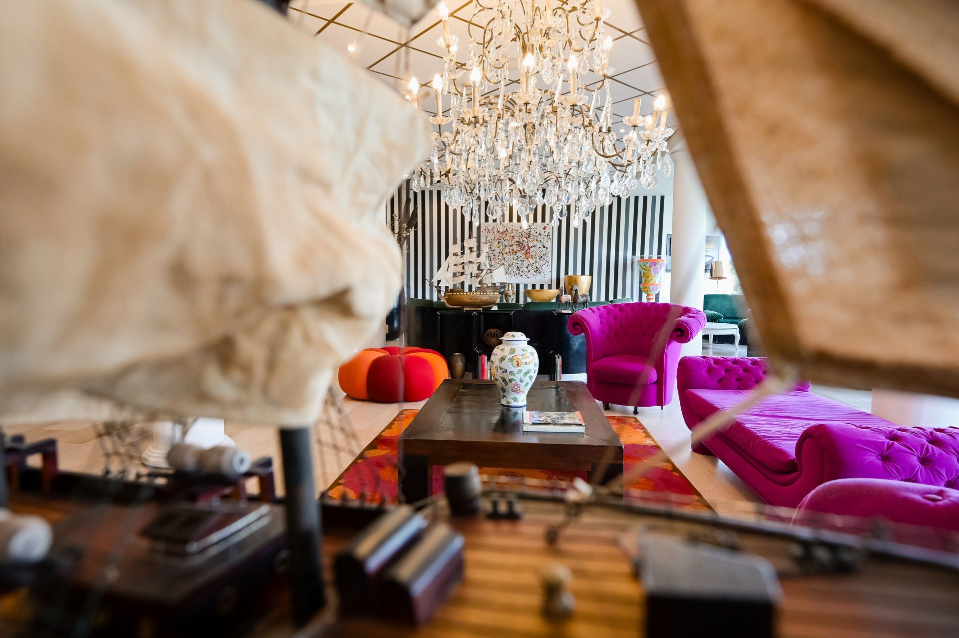 Lussuoso salotto con lampadario di cristallo, sedute rosse e magenta e un tavolino da caffè lucido.
