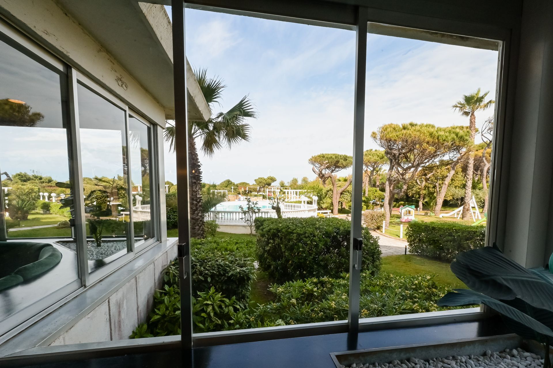 Vista da un patio coperto di un giardino, palme e un porto turistico in lontananza, in piena luce del giorno.
