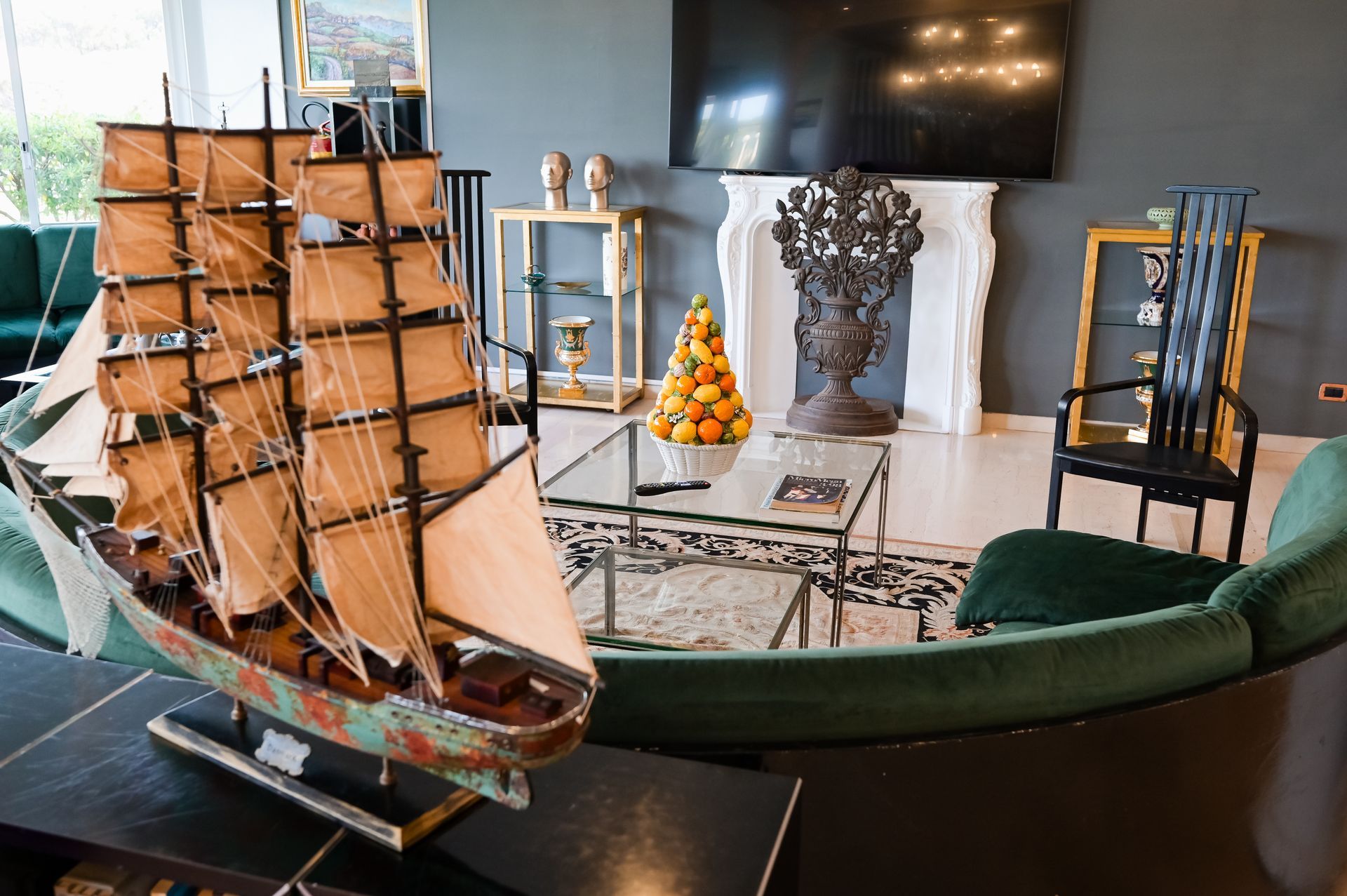 Esposizione di modellini di navi in ​​una stanza con TV, sedia verde e scultura decorativa su un tavolo.