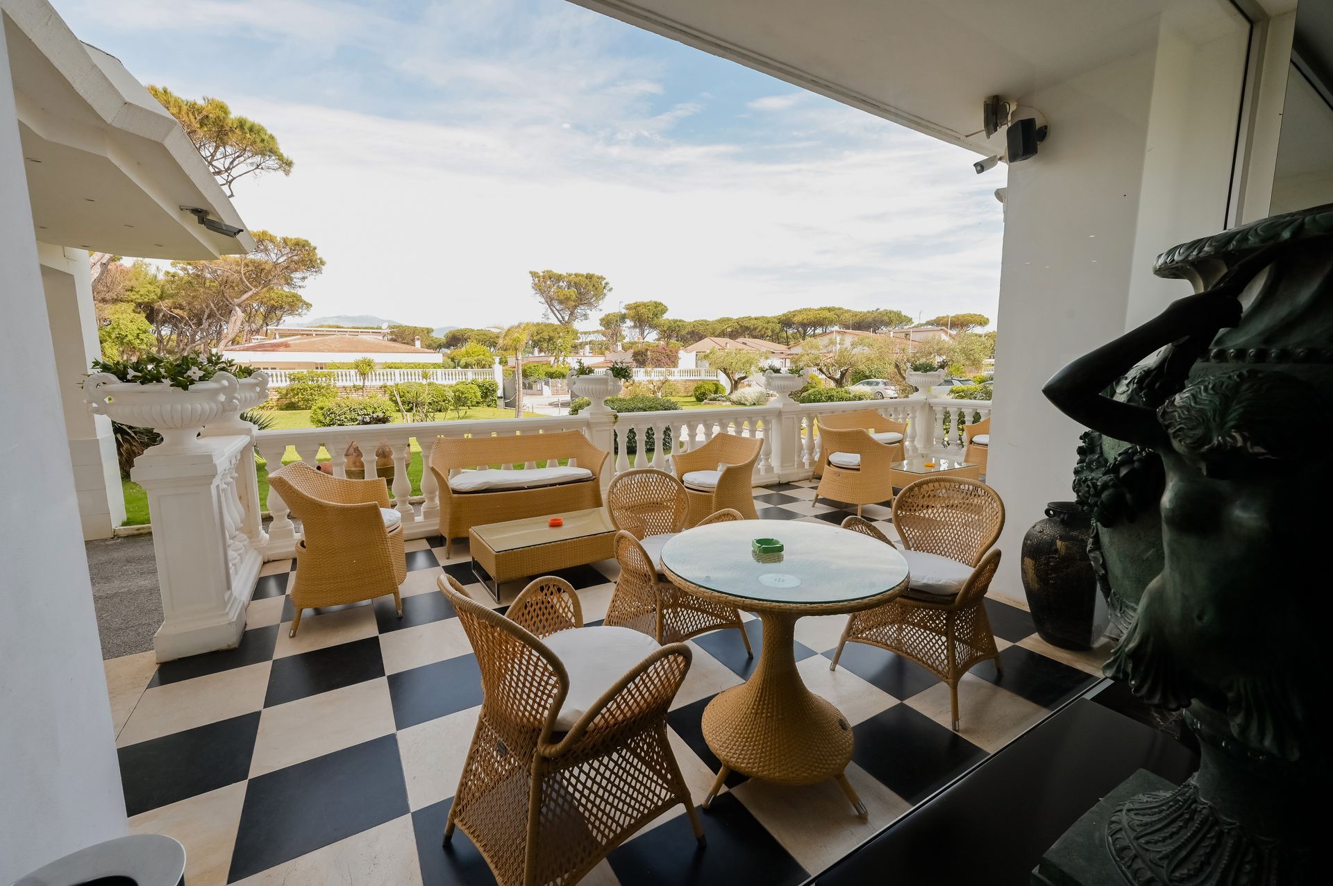Patio coperto con sedie in vimini, tavolo rotondo, pavimento in bianco e nero e vista sull'oceano oltre la ringhiera.