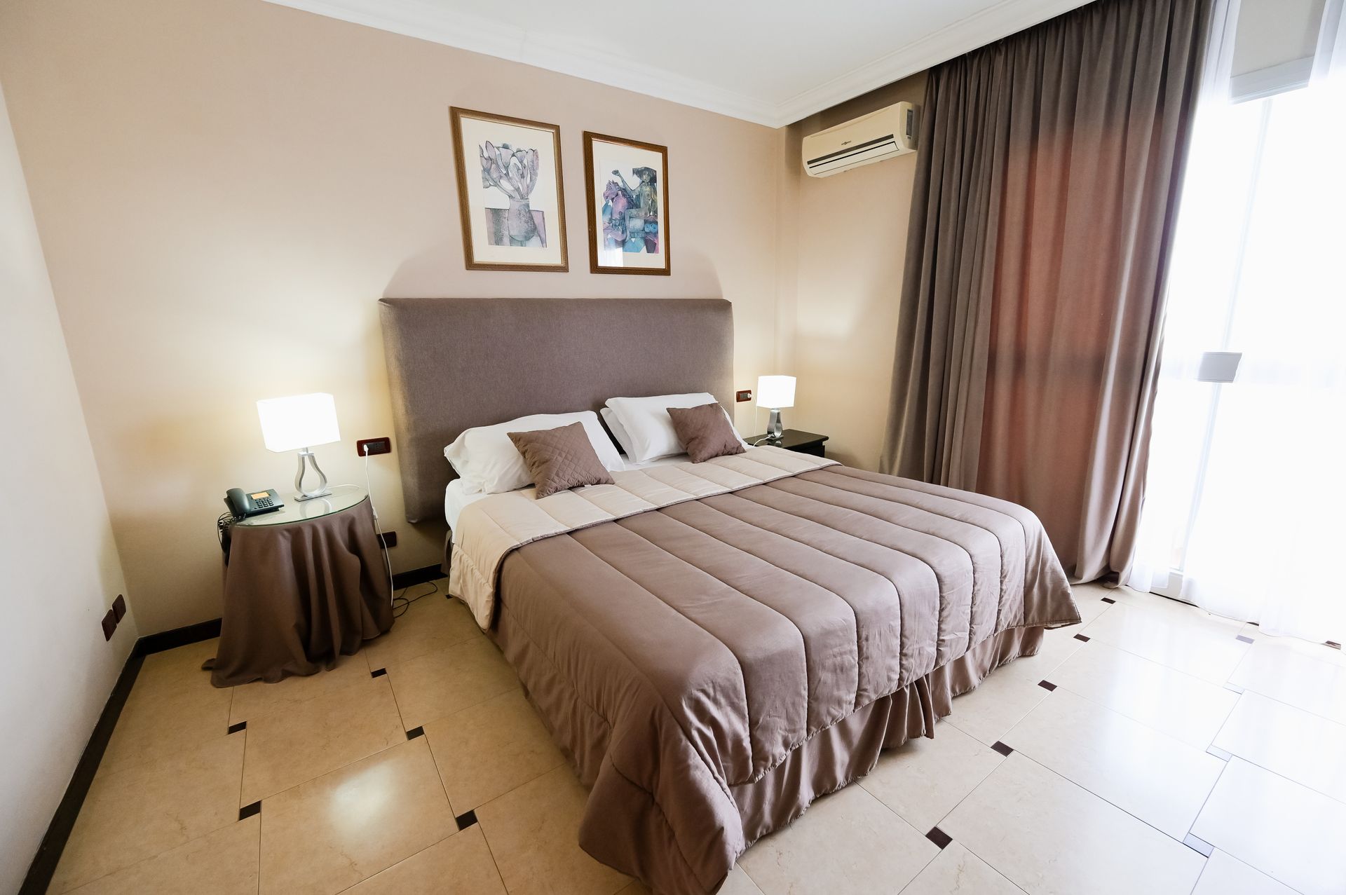 Camera da letto moderna con letto king size, lampade da comodino, quadri incorniciati e tende a tutta altezza.