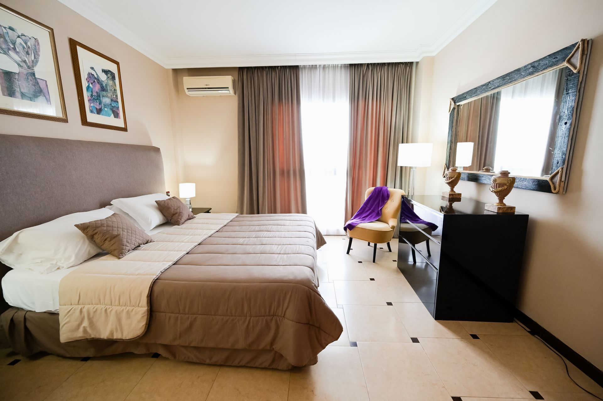 Camera d'albergo moderna con letto king size, scrivania vicino alla finestra, grande specchio e arredamento dai toni neutri.