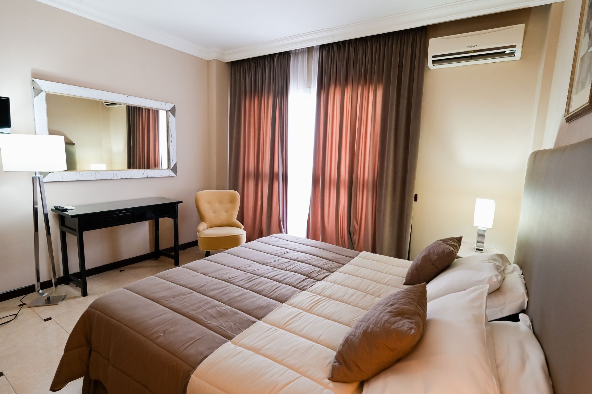 Camera da letto moderna con letto, scrivania, specchio, sedia e tende accanto a un condizionatore a parete.