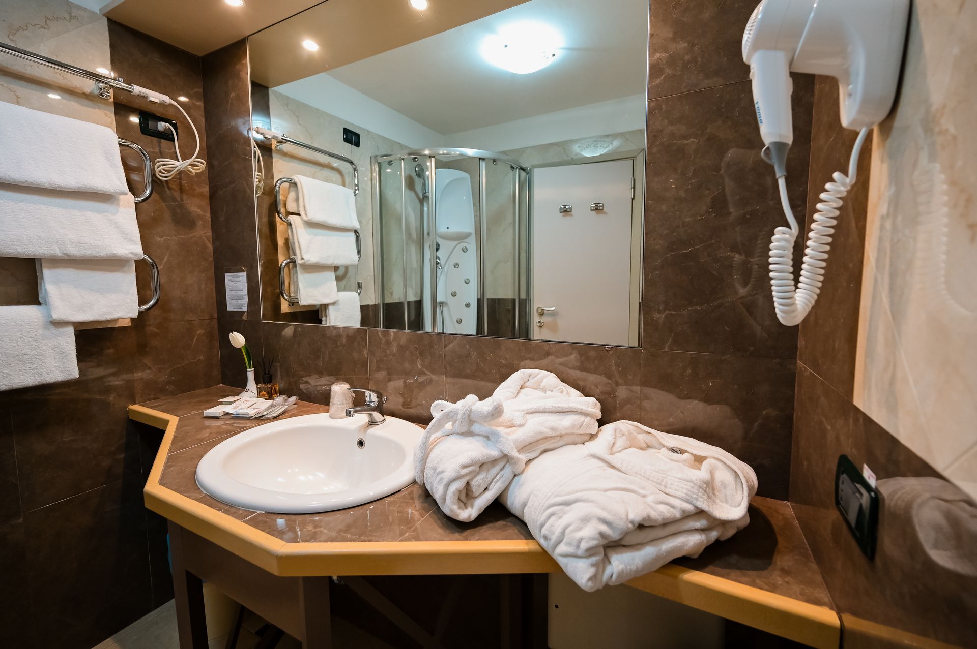 Bagno moderno dell'hotel con lavabo, specchio, asciugamani, doccia e asciugacapelli a parete.