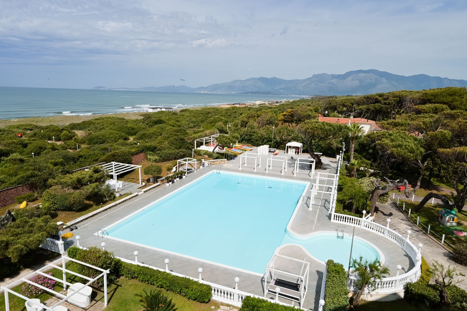 Piscina all'aperto con lettini bianchi con vista sull'oceano e sulle montagne in lontananza.